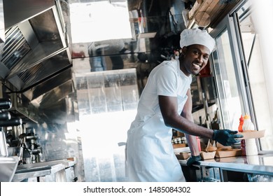 Selective Focus Of Cheerful African American Chef Smiling While Holding Carton Plate In Food Truck 