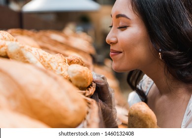 selective focus of cheerful asian woman smiling while smelling bread in supermarket  - Powered by Shutterstock