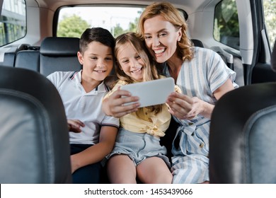 Selective Focus Of Cheerful Family Taking Selfie On Smartphone In Car 