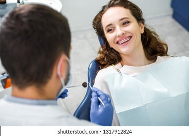 selective focus of cheerful woman in braces during examination of teeth near dentist