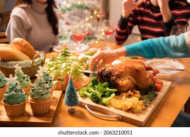 El foco selectivo de la cena navideña en la mesa con la mano puso un pequeño árbol de Navidad junto a un pavo asado con brócoli y papas, apetitoso fácil, quequitos de árbol de Navidad, pan en Nochebuena.