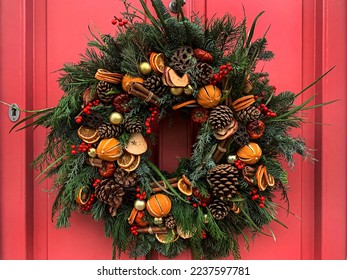 Selective focus of Christmas wreath. Festive christmasy themed winter natural wreath on a pink wooden door, decorated with lotus, pine cones, oranges, vanilla stick. Red berries. Festive mood. - Powered by Shutterstock
