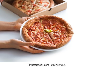 Selective focus of the circle of pepperoni pizza on a plate in the boy's hands. The concept of a snack for children, take off, take away.