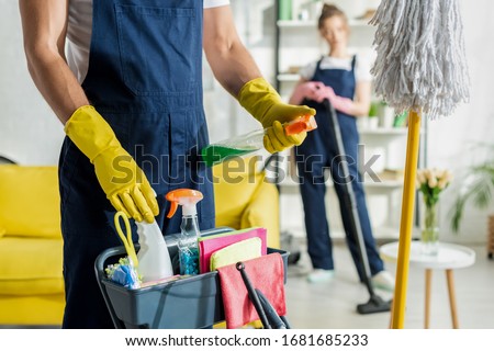 selective focus of cleaner holding spray bottle near cleaning trolley