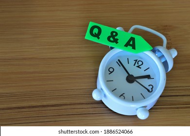 Selective focus of clock and memo note written with text Q and A over wooden background. Business concept.