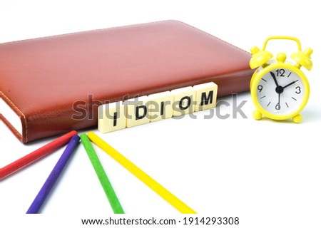 Selective focus of clock, notebook, wooden sticks and scrabble letters with text IDIOM