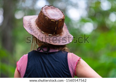 Selective focus close up on back view of woman wearing cowboy leather hat as she looking forward, with copy space and blurred background of nature