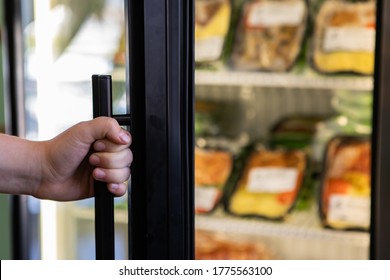 Selective Focus And Close Up View Of Hand Holding The Refrigerator Handle In The Supermarket, Blurred Food Products In Background. With Copy Space.