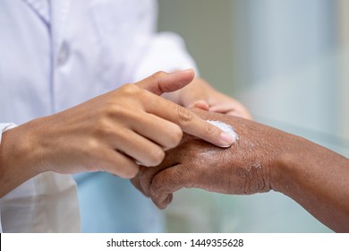 Selective focus close up woman pharmacist or doctor hand apply steroid moisturizer cream on old asian man hand with flaking dry itchy skin conditions peeling by allergic dermatitis.