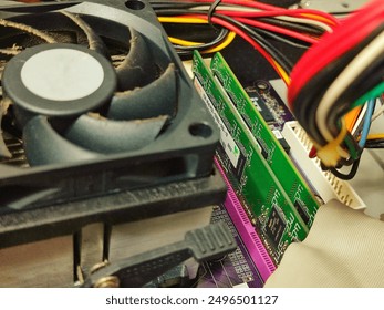 selective focus and close-up of the components inside a computer desktop. there are wires of various colors, white sockets, purple and green circuit boards, black cooling fans and various other types 
