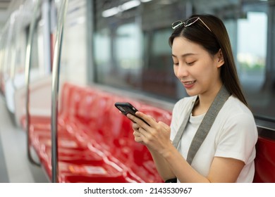 Selective focus and close-up of a happy Asian female traveler sitting on an empty red row chair in an electric train, smiling using a cellphone while traveling by the sky train. Copy space on the left