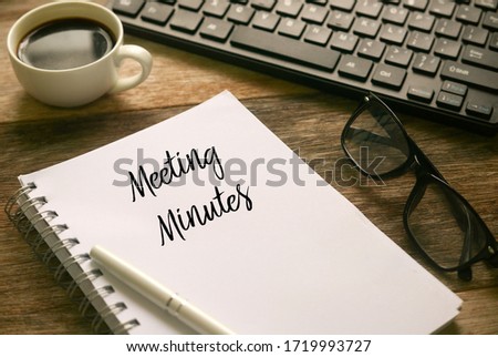 Selective focus of coffee,computer keyboard,glasses,pen and notebook written with Meeting Minutes on wooden background.