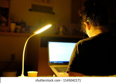 Selective focus of concentrated asian young phd student using computer for studying and writing in the evening at her room. Work at night in the dark room. Social Distancing home quarantine Covid-19.