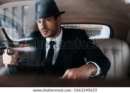 Selective focus of confident mafioso holding gun in car