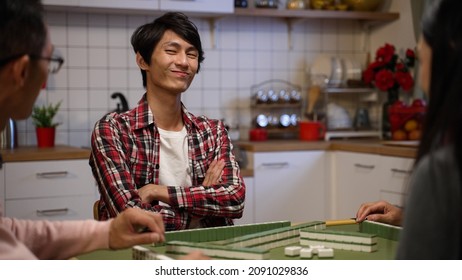 selective focus of confident son wearing a shirt sitting and smiling with folded arms and funny face after drawing and laying down a mahjong tile on the table on chinese new year