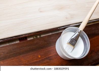 Selective focus. A container with paint and a brush. The horizontal boards are painted with white paint and a brush. Renovation and design. Place for your text. Copy space.