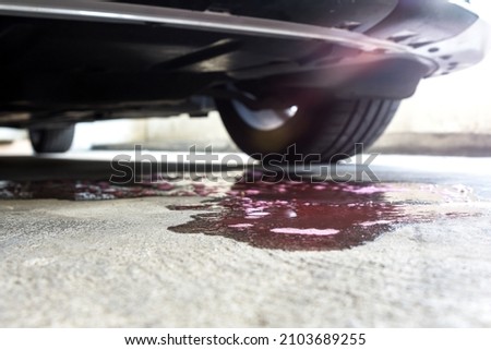 Selective focus of coolant liquid leak out from the engine down on the floor on blurred  Car parked background.