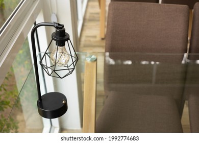 Selective Focus With Copy Space Shot Of Vintage Lamp And Edison Style Light Bulb On Glass Table With Chairs In The Room Near Window Of Restaurant Shows Contemporary Style Decoration.