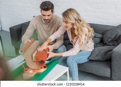 Selective Focus Of Couple Wrapping Christmas Gift Box Together In Living Room