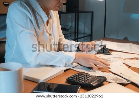 Selective focus of cropped view of Asian female accountant in white shirt sitting at desk full of receipts and calculator, are collecting and classified receipts for calculating expenses in an office.