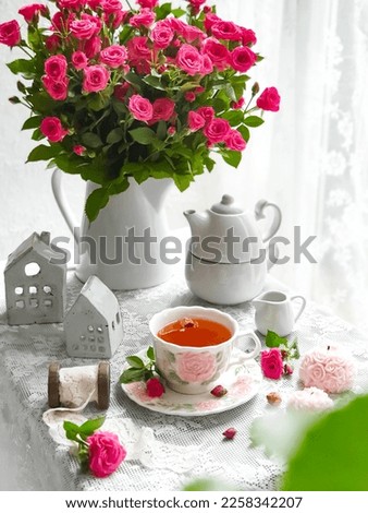 Selective focus of cup of tea with pink baby rose flowers on white table and white background.