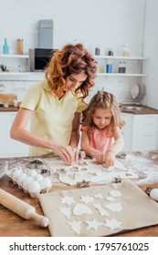 selective focus of curly mother and blonde daughter cutting out cookies from rolled dough