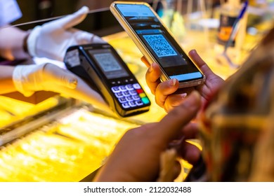 Selective focus to customer hand using smart phone to scan Qr code payment tag  on credit card machine with blurry gold background in gold jewelry shop to accepted generate digital pay without money. 