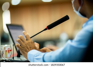 Selective Focus To Desktop Wireless Conference Microphones With Blurry Businessman Wearing Mask In A Meeting Room, Microphone On The Desk In Meeting Room With Blurry Speaker. The Concept Of Speaking.