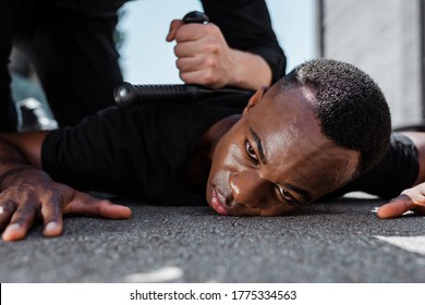 selective focus of detained african american man lying on ground near police officer with baton, racism concept