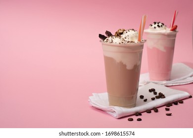 Selective focus of disposable cups of chocolate and strawberry milkshakes with coffee grains on napkins on pink background