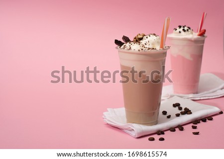 Selective focus of disposable cups of chocolate and strawberry milkshakes with coffee grains on napkins on pink background