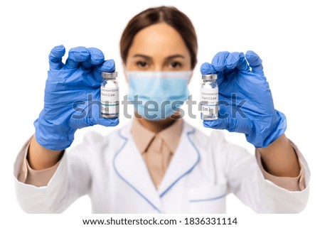 Selective focus of doctor in latex gloves holding jars with coronavirus vaccine lettering isolated on white