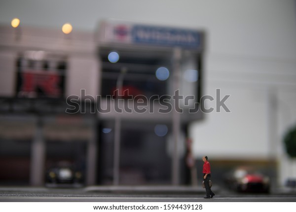 Selective focus of doll figure adult\
man walk along pedestrian walkway with blurred\
background.