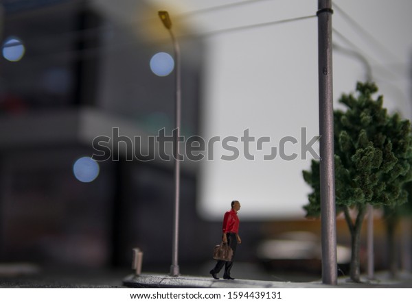 Selective focus of doll figure adult\
man walk along pedestrian walkway with blurred\
background.