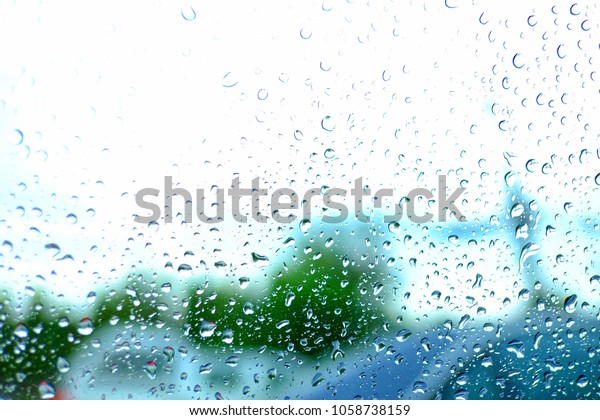 In\
selective focus of droplets on the car window with blurred white\
sky in the rainy day and green trees on the sideway\

