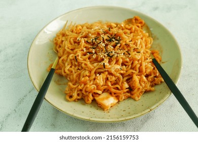 Selective focus dry (no soup) spicy Korean instant noodles with chopsticks on plate, with white background. Samyang ramen noodles topped with sesame and seaweed. 