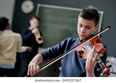 Selective focus dutch angle shot of modern teen boy playing violin during music class at school