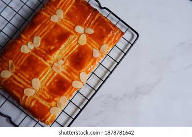 Selective Focus Of Dutch Style Of Butter Cake Named Holland Boterkoek With Almond Slices Topping In A Wire Rack In White Background