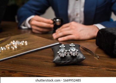 Selective focus of earrings on jewelry pillow and jewelry appraiser working at table in workshop