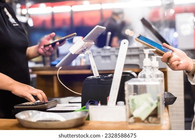 Selective focus to edge of smartphone in hand with blurry the tablet and cashier staff using it to receive orders from customers at counter service in cafe or store. - Powered by Shutterstock