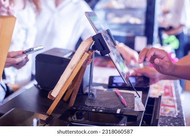 Selective focus to edge of the tablet with blurry cashier staff using tablet to receive orders from customers at counter service in cafe or store.