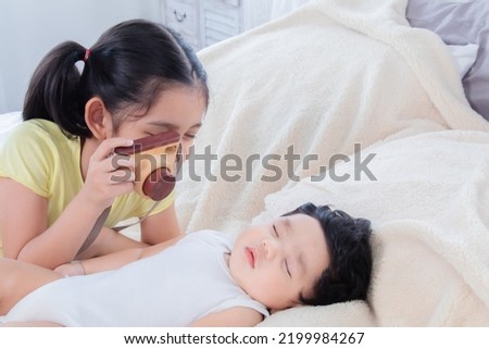 Selective focus elder sister teasing newborn baby while sleeping on bed. Happy adorable girl using toy camera take a photo little boy while lying on bed together. happy family relationships concept.