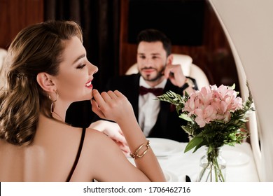 selective focus of elegant man looking at attractive woman while sitting at served table in plane