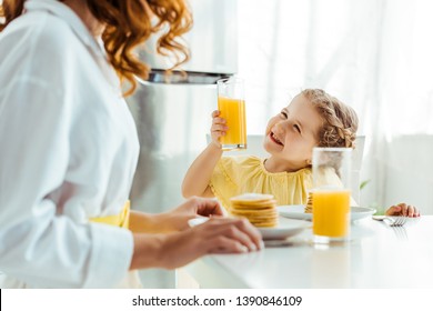 selective focus of emotional happy daughter looking at mother and holding glass with orange juice while having breakfast - Powered by Shutterstock