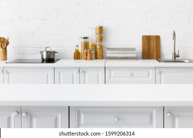 selective focus of empty tabletop and minimalistic modern white kitchen interior with kitchenware and food near brick wall on background - Powered by Shutterstock