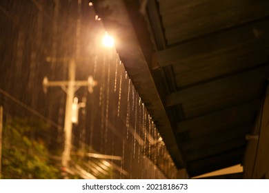 selective focus at the end of the roof tile raining at night electric pole background orange light gives a feeling of loneliness on a rainy day. Look up at the rain at the end of the roof. Leave space