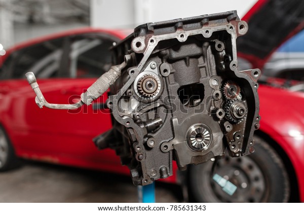 Selective focus. Engine\
Block on a repair stand with Piston and Connecting Rod of\
Automotive technology. Blurred red car on background. Interior of a\
car repair shop.