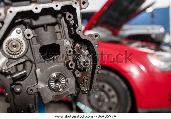 Selective focus. Engine\
Block on a repair stand with Piston and Connecting Rod of\
Automotive technology. Blurred red car on background. Interior of a\
car repair shop.