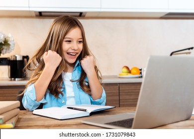 selective focus of excited kid gesturing and looking at laptop while e-learning at home