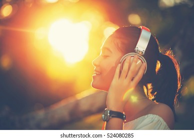 Selective Focus Of Eyebrow. Portrait Of Asian Young Woman With Headphones And Listening Music On Sunset In Park.